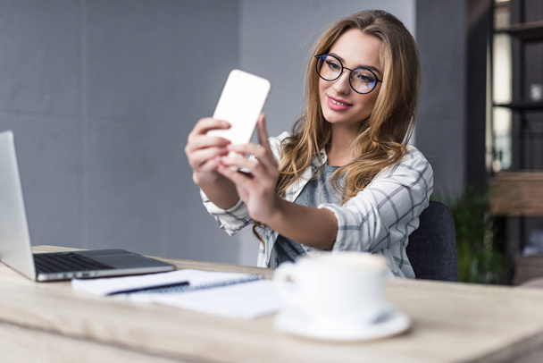 smiling young businesswoman taking selfie at workplace - Photo, Image