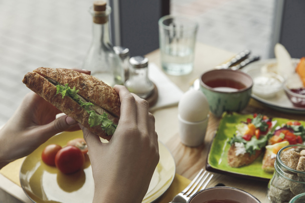 cropped shot of person eating fresh tasty sandwich at breakfast  - Фото, изображение