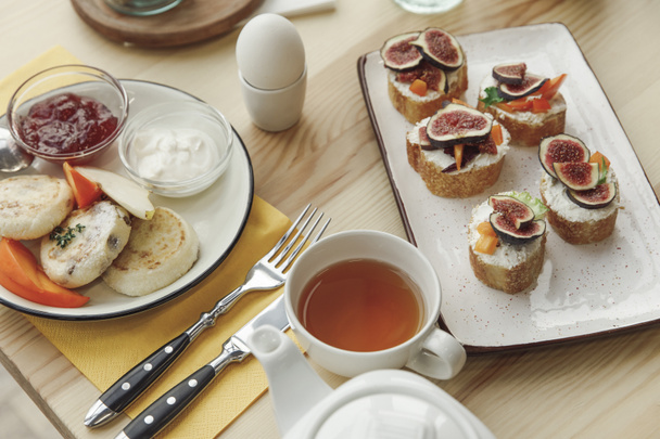 close-up view of tasty healthy breakfast with cheesecakes fritters and canapes with figs on table  - Foto, imagen