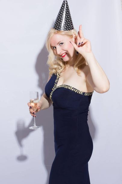 Beautiful young blond woman at the party. The girl is dressed in evening dress with a festive cap, in her hand holds a glass of champagn - Foto, afbeelding