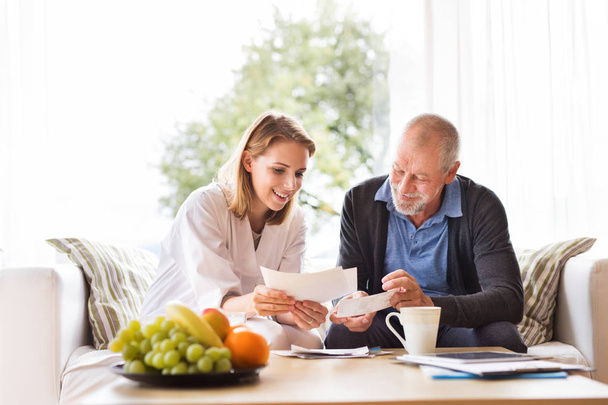Health visitor and a senior man with tablet during home visit. - Foto, Bild