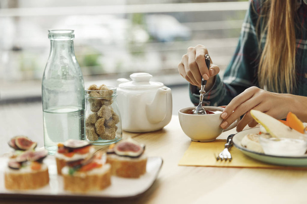 tiro cortado de menina bebendo chá enquanto toma café da manhã
 - Foto, Imagem