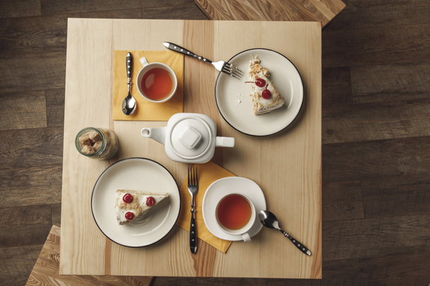vue sur le dessus de la bouilloire, deux tasses avec thé chaud et délicieuses pâtisseries sur la table
  - Photo, image