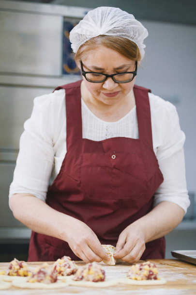 Aikuinen nainen lasit ja esiliina leipoo kakkuja leipomon kasvot
 - Valokuva, kuva