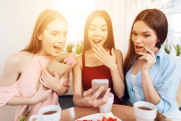 Three girls look at the smartphone screen, celebrating the holiday on March 8. - Foto, Imagem