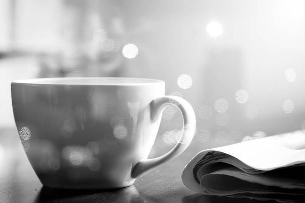 Гаряча кава в білій чашці і газета на дерев'яному столі і ранкове світло сяє. Монотонний ефект
. - Фото, зображення