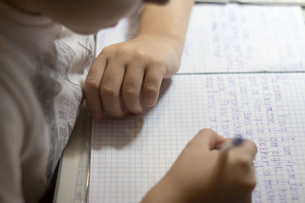 Close-up van de hand van de jongen met potlood schrijven van Engelse woorden met de hand op papier van de traditionele witte Kladblok. - Foto, afbeelding