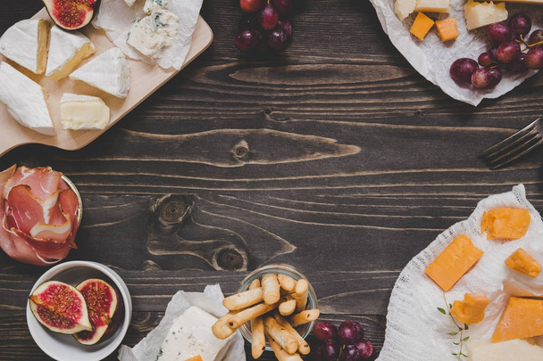 Cheese selection with fruits and snacks on the wooden dark table with copy space. Top view background - Foto, Imagem