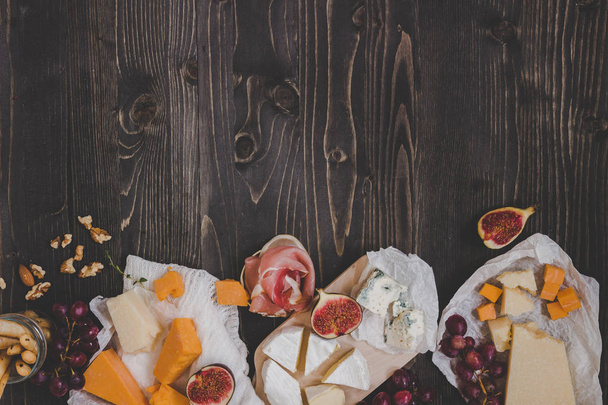 Various types of cheese with fruits and snacks on the wooden dark table with copy space - Fotó, kép