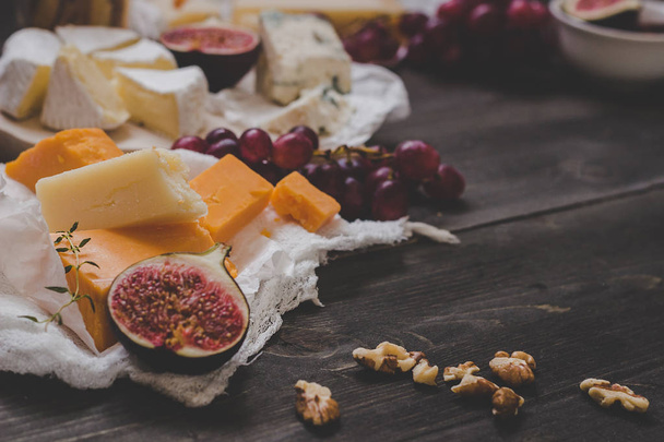 Various types of cheese with fruits and nuts on the wooden dark table. Selective focus - Foto, Imagen