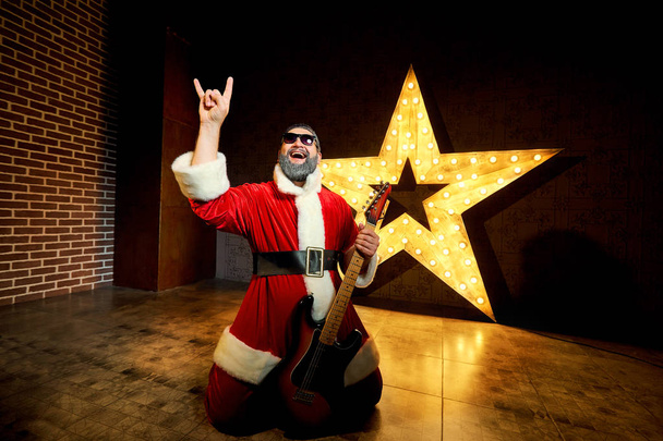 Happy Santa with a guitar is dancing against the background of a - Fotografie, Obrázek