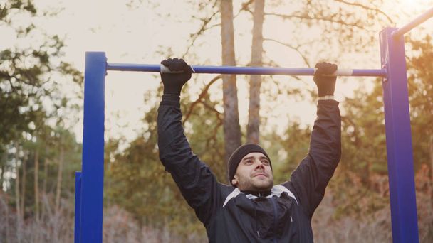 Jeune homme athlétique faisant de l'exercice pull-up dans le parc d'hiver en plein air
 - Photo, image