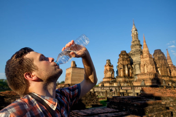 Nuori mies janoinen juo pullotettua vettä buddhalaisuudessa temppeli Thaimaassa
 - Valokuva, kuva