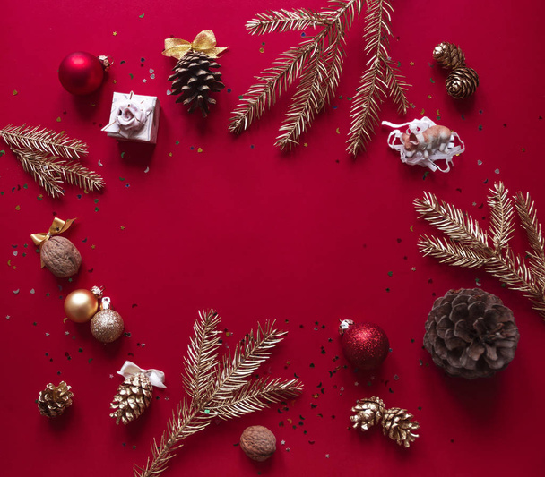 On a red raspberry background, the Christmas and New Year decorations and gilded branches of the Christmas tree are arranged in a circle - Foto, Imagen