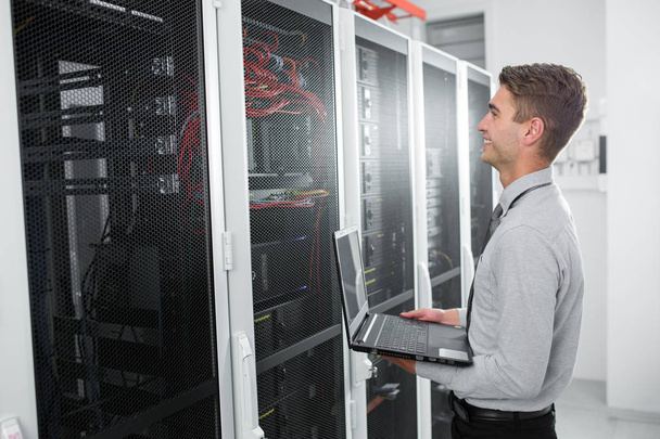 Portrait of modern young man holding laptop standing in server room working with supercomputer - Φωτογραφία, εικόνα