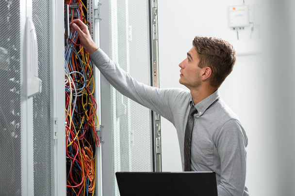 Portrait of modern young man holding laptop standing in server room working with supercomputer - Фото, изображение