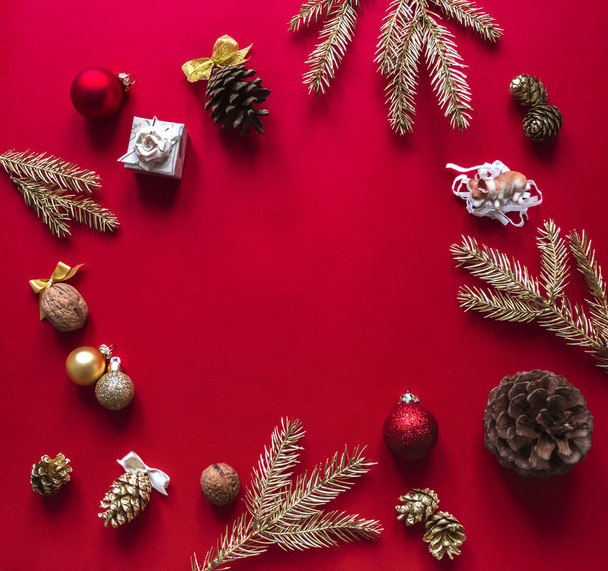 On a red raspberry background, the Christmas and New Year decorations and gilded branches of the Christmas tree are arranged in a circle - Foto, Imagen