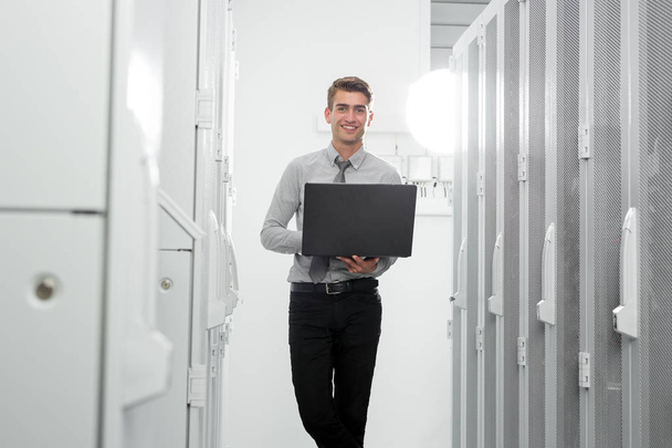 Portrait of modern young man holding laptop standing in server room working with supercomputer - Фото, зображення