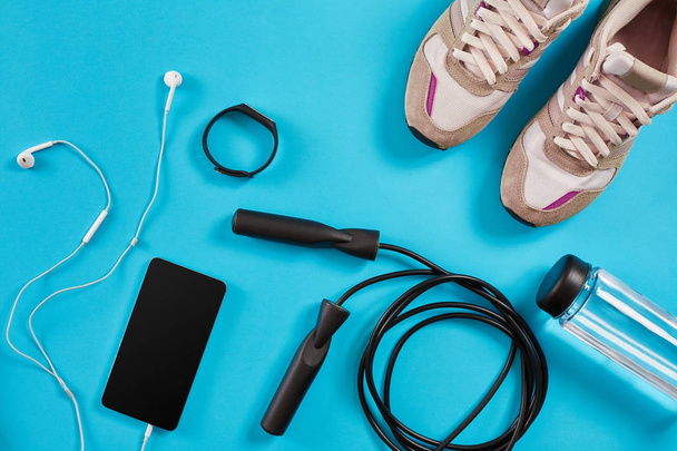 Flat lay shot of Sport equipment. Sneakers, jump rope, earphones and phone on blue background. - Photo, Image