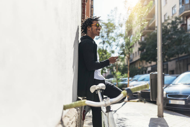 Afro young man using mobile phone and fixed gear bicycle. - Φωτογραφία, εικόνα