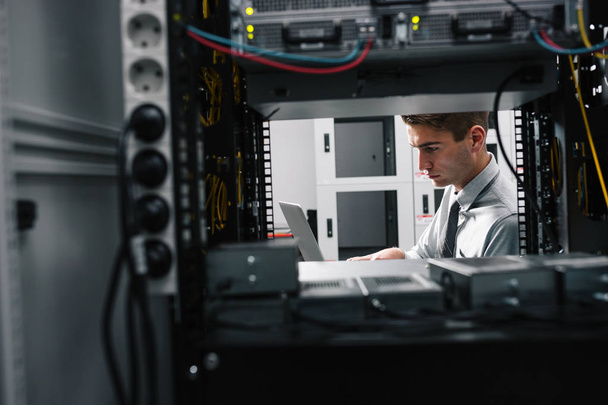 Portrait of modern young man holding laptop standing in server room working with supercomputer - Foto, Imagem