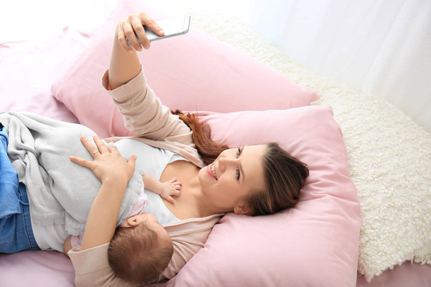 Young mother taking selfie with baby on bed at home - Φωτογραφία, εικόνα