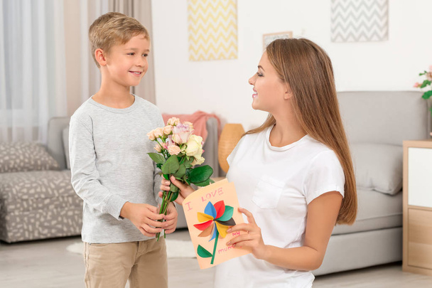 Young woman receiving flowers and card from her little son on Mother's Day at home - Foto, immagini