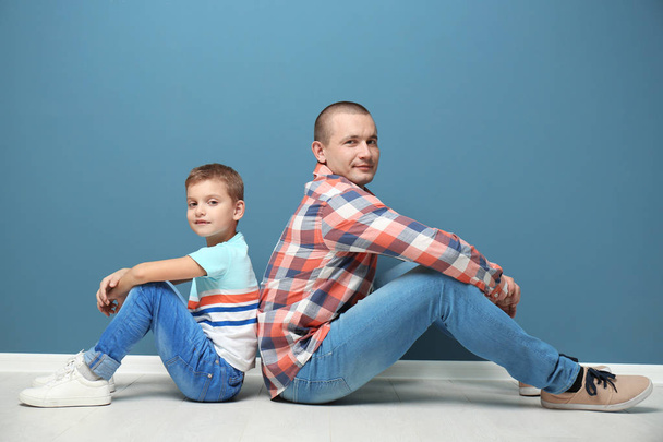 Dad and his son sitting on floor near color wall - Φωτογραφία, εικόνα