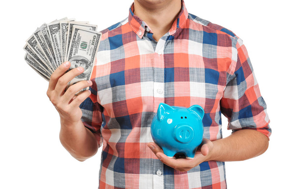 Young man with dollar bills and piggy bank on white background, closeup - Photo, Image