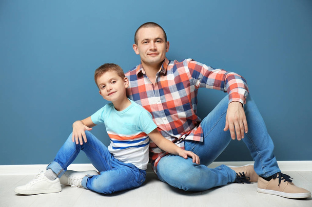 Dad and his son sitting on floor near color wall - Φωτογραφία, εικόνα