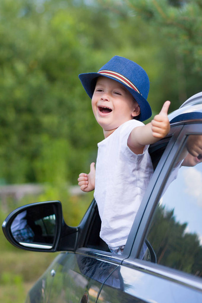 Boy in hat looks out of car window and shows thumbs up - Fotoğraf, Görsel
