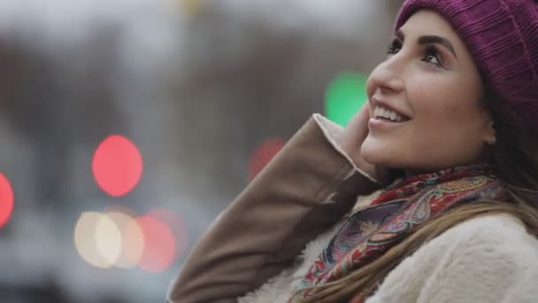 Young happy woman in violet hat looking up and smiling at camera in a city - Кадры, видео