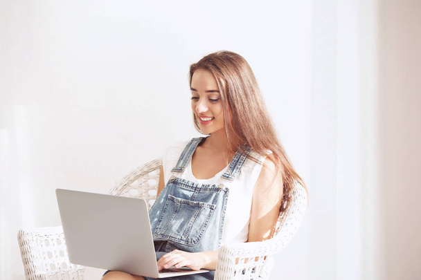 Young woman using laptop while sitting in armchair indoors - Foto, Bild