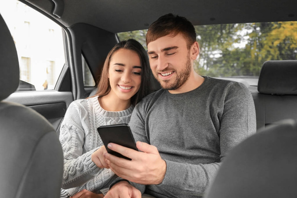 Happy young couple with mobile phone on back seat of taxi car - Foto, Imagem