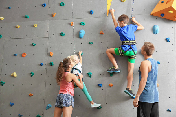 Instructors helping children climb wall in gym - Foto, afbeelding