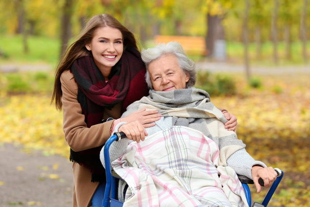 Disabled senior woman and young caregiver in park - Foto, imagen