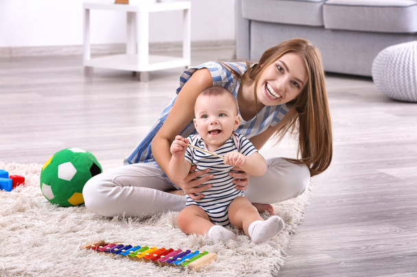 Young mother and cute baby playing on floor at home - Фото, изображение