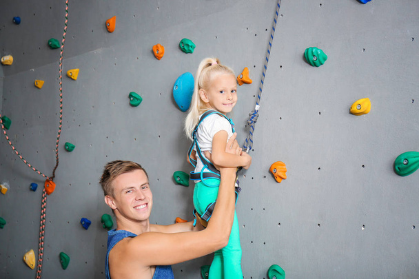 Instructor helping little girl climb wall in gym - Photo, Image