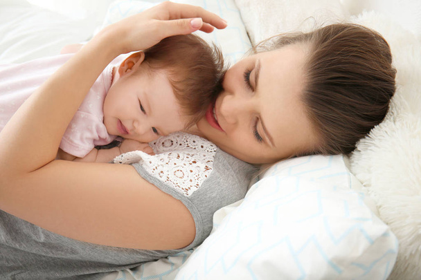 Young mother holding cute little baby on bed at home - Photo, Image
