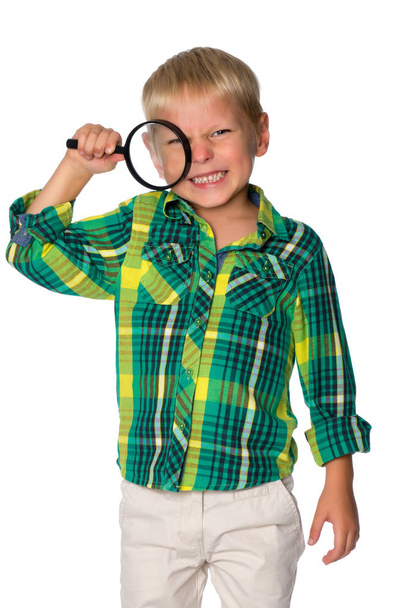 A small boy looks through a magnifying glass. - Фото, зображення