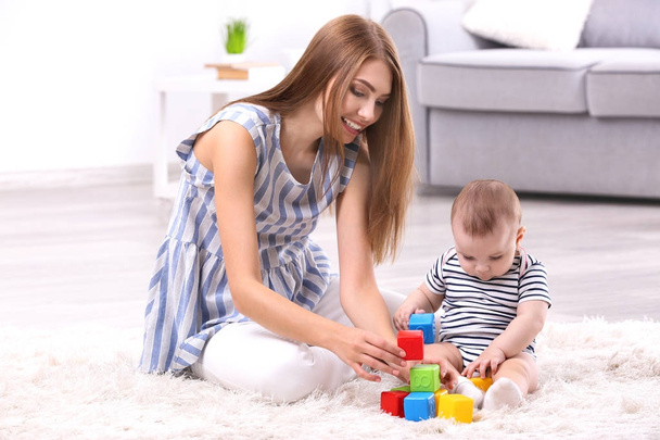 Young mother and cute baby playing on floor at home - Foto, afbeelding