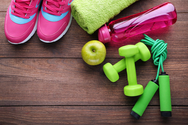Pink bottle, green apple, dumbbells and skipping rope on wooden table - Photo, Image