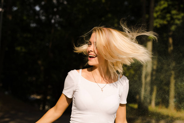 Χαρούμενη νεαρή γυναίκα στο λευκό t shirt με φτερουγίσματα μαλλιά ποζάρει  - Φωτογραφία, εικόνα