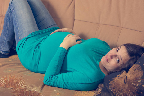έγκυος γυναίκα που στηρίζεται σε έναν καναπέ. - Φωτογραφία, εικόνα