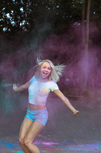 Preciosa mujer joven saltando con Holi polvo explotando a su alrededor
 - Foto, Imagen