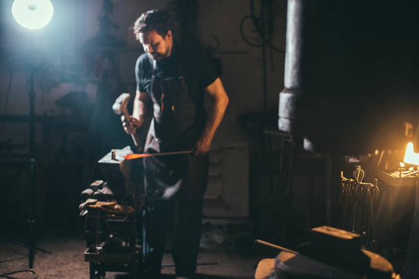 Senior blacksmith forging molten metal on the anvil in smithy. - Foto, Bild