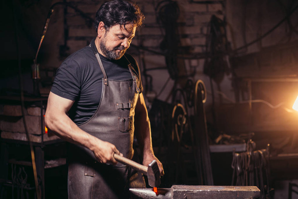 blacksmith manually forging molten metal on anvil in smithy with spark fireworks - Fotó, kép