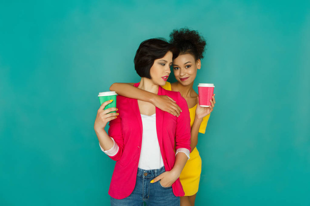 Two girlfriends drinking coffee at turquoise studio background - Photo, Image