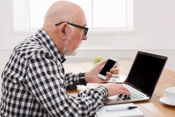 Hombre mayor usando portátil y maqueta de teléfonos inteligentes
 - Foto, Imagen