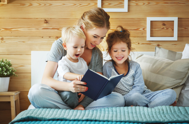 family mother reading to  children book in be - Фото, изображение